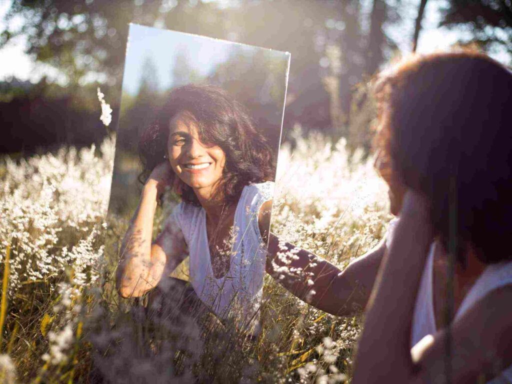 jeune femme dans un champ en train de sourire dans le miroir