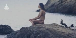 Jeune homme aux cheveux longs en train de méditer au bord de l'eau