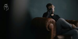 Homme anxieux assis sur un sofa qui se prend la tête dans ses mains