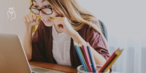 Jeune femme devant son ordinateur qui mord son stylo