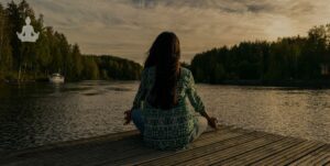 jeune femme face à un lac en train de méditer