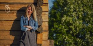 Femme se tenant devant une maison en bois et qui sourit